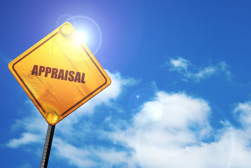 A yellow road sign which reads "appraisal" against white clouds and a blue sky.